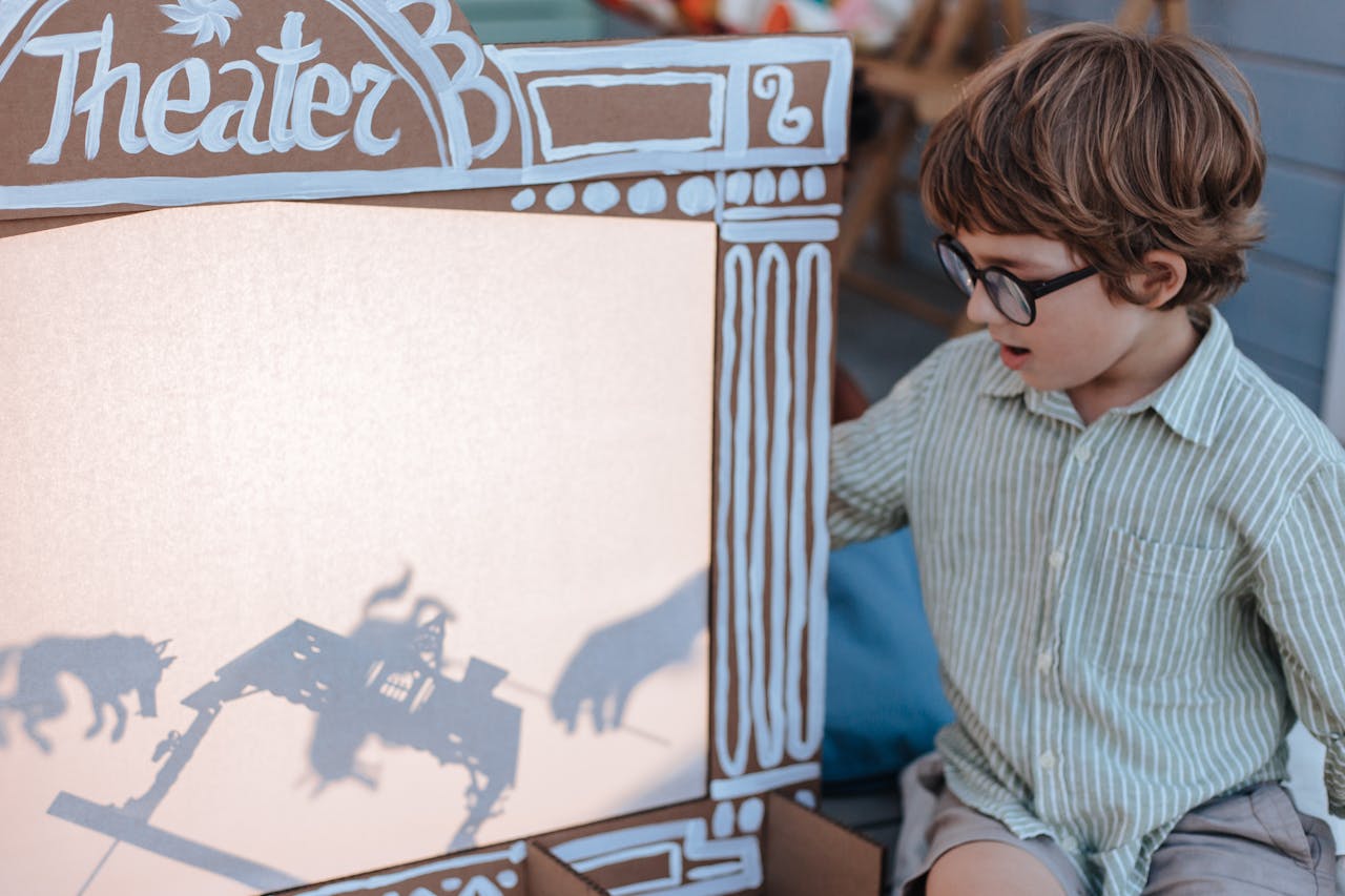 A young boy with glasses playing with a shadow puppet theater indoors.