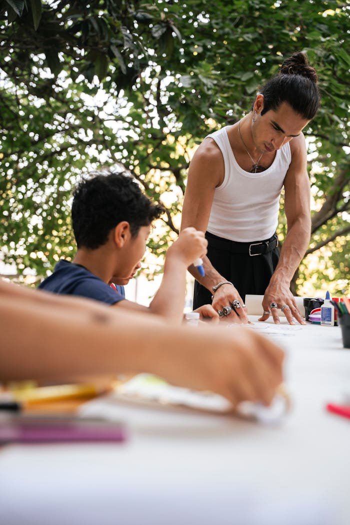 Art teacher guides student in outdoor drawing class under a tree.
